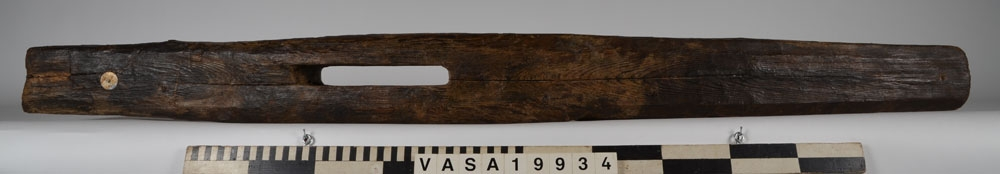 Bordklämma. Del av bordklämma bestående av den ena armen - eller käften. De ursprungliga kanterna och ändarna är i huvudsak väl bevarade. 840 mm från framänden finns  ett genomgående avlångt hål för tvärbrädan som håller ihop de två armarna. Eftersom märgen har lämnats kvar i ämnet har det bildats en märgspricka som löper längs översidans hela längd. Översidans kanter är fasade. Fasningens bredd är ca 25-30 mm. Ett genomgående, fyrkantigt spikhål med avtryck efter skalle på översidan, finns ca 55 mm från den smala ändens kant.  Verktygsspår på översidan, sannoligt av bilyxa. På den lätt välvda undersidan syns verktygsspår som troligen härrör  från en mer korteggad yxa. Det är gott om omotiverade och slumpvisa huggskador efter yxa, precis som om bordklämman vid något tillfälle har använts som huggkubbe. Föremålet är ganska oanfrätt.

För mer information se Dokumentationsblankett under Referenser – Länkade filer.