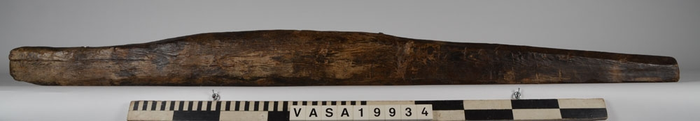 Bordklämma. Del av bordklämma bestående av den ena armen - eller käften. De ursprungliga kanterna och ändarna är i huvudsak väl bevarade. 840 mm från framänden finns  ett genomgående avlångt hål för tvärbrädan som håller ihop de två armarna. Eftersom märgen har lämnats kvar i ämnet har det bildats en märgspricka som löper längs översidans hela längd. Översidans kanter är fasade. Fasningens bredd är ca 25-30 mm. Ett genomgående, fyrkantigt spikhål med avtryck efter skalle på översidan, finns ca 55 mm från den smala ändens kant.  Verktygsspår på översidan, sannoligt av bilyxa. På den lätt välvda undersidan syns verktygsspår som troligen härrör  från en mer korteggad yxa. Det är gott om omotiverade och slumpvisa huggskador efter yxa, precis som om bordklämman vid något tillfälle har använts som huggkubbe. Föremålet är ganska oanfrätt.

För mer information se Dokumentationsblankett under Referenser – Länkade filer.