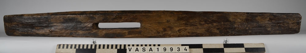 Bordklämma. Del av bordklämma bestående av den ena armen - eller käften. De ursprungliga kanterna och ändarna är i huvudsak väl bevarade. 840 mm från framänden finns  ett genomgående avlångt hål för tvärbrädan som håller ihop de två armarna. Eftersom märgen har lämnats kvar i ämnet har det bildats en märgspricka som löper längs översidans hela längd. Översidans kanter är fasade. Fasningens bredd är ca 25-30 mm. Ett genomgående, fyrkantigt spikhål med avtryck efter skalle på översidan, finns ca 55 mm från den smala ändens kant.  Verktygsspår på översidan, sannoligt av bilyxa. På den lätt välvda undersidan syns verktygsspår som troligen härrör  från en mer korteggad yxa. Det är gott om omotiverade och slumpvisa huggskador efter yxa, precis som om bordklämman vid något tillfälle har använts som huggkubbe. Föremålet är ganska oanfrätt.

För mer information se Dokumentationsblankett under Referenser – Länkade filer.