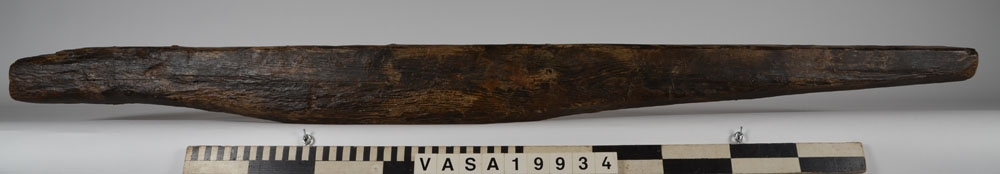Bordklämma. Del av bordklämma bestående av den ena armen - eller käften. De ursprungliga kanterna och ändarna är i huvudsak väl bevarade. 840 mm från framänden finns  ett genomgående avlångt hål för tvärbrädan som håller ihop de två armarna. Eftersom märgen har lämnats kvar i ämnet har det bildats en märgspricka som löper längs översidans hela längd. Översidans kanter är fasade. Fasningens bredd är ca 25-30 mm. Ett genomgående, fyrkantigt spikhål med avtryck efter skalle på översidan, finns ca 55 mm från den smala ändens kant.  Verktygsspår på översidan, sannoligt av bilyxa. På den lätt välvda undersidan syns verktygsspår som troligen härrör  från en mer korteggad yxa. Det är gott om omotiverade och slumpvisa huggskador efter yxa, precis som om bordklämman vid något tillfälle har använts som huggkubbe. Föremålet är ganska oanfrätt.

För mer information se Dokumentationsblankett under Referenser – Länkade filer.