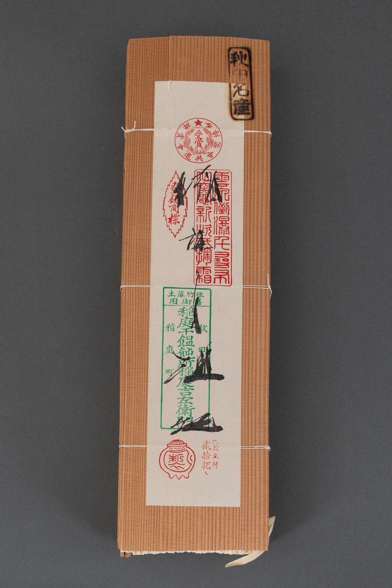 Pakning laget av to tynne plater i japanseder, med smalere plater på sidene, ombundet med tre tynne snorer. På den ene platen er det et svimerke og en påklistret papiretikett. I pakningen ligger tørkede nudler ombundet med tre bånd.