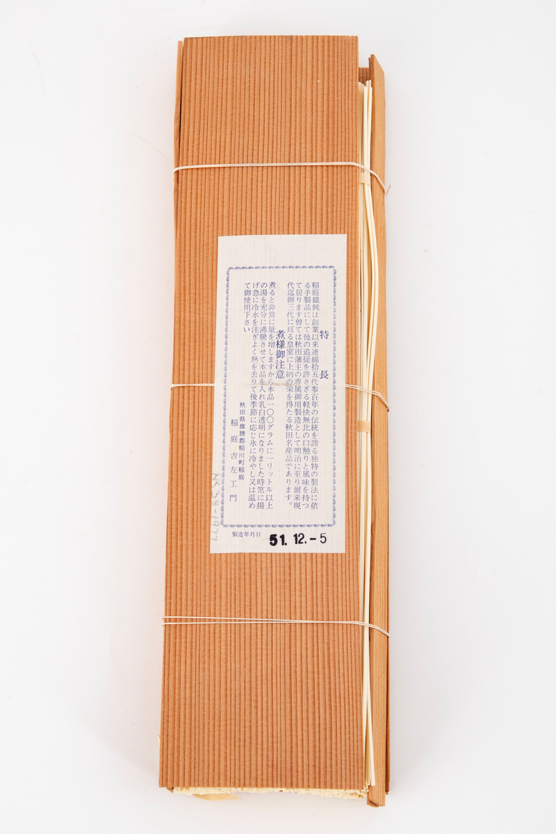 Pakning laget av to tynne plater i japanseder, med smalere plater på sidene, ombundet med tre tynne snorer. På den ene platen er det et svimerke og en påklistret papiretikett. I pakningen ligger tørkede nudler ombundet med tre bånd.