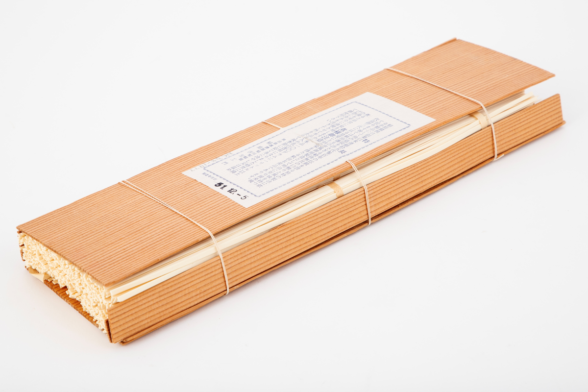 Pakning laget av to tynne plater i japanseder, med smalere plater på sidene, ombundet med tre tynne snorer. På den ene platen er det et svimerke og en påklistret papiretikett. I pakningen ligger tørkede nudler ombundet med tre bånd.