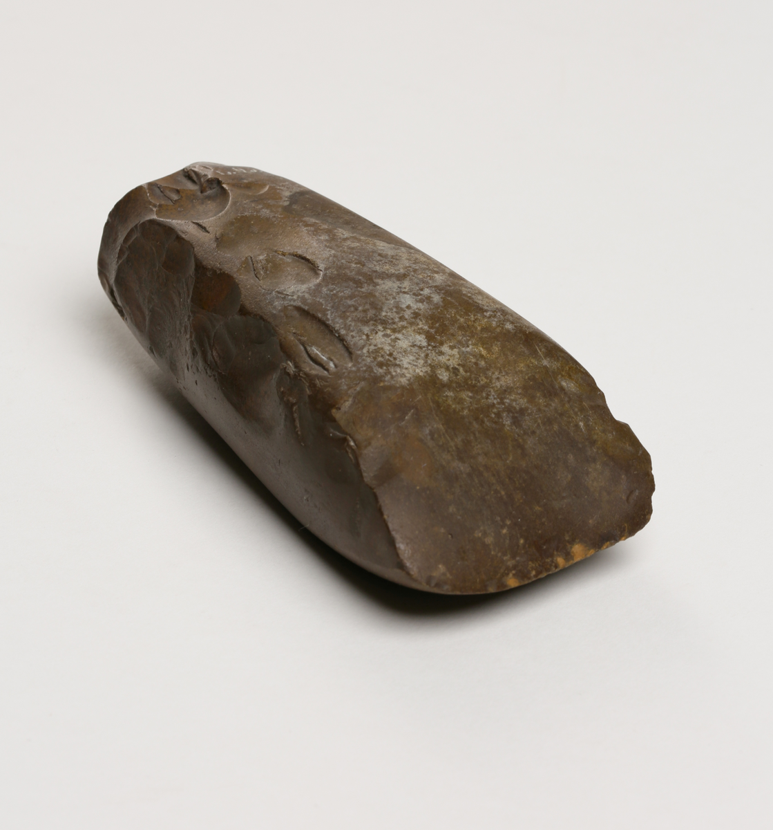 Flintyxa av brun flinta, tjocknackig, slipad och svallad, svagt håleggad. Kvadratisk genomskärning.