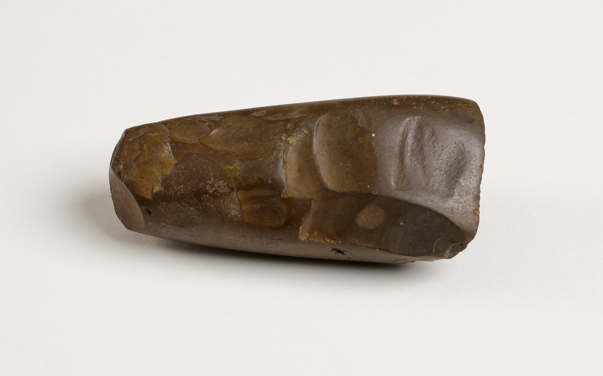 Flintyxa av brun flinta, tjocknackig, slipad och svallad, svagt håleggad. Kvadratisk genomskärning.