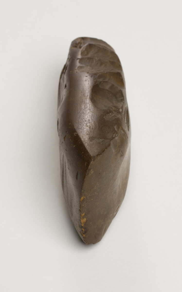 Flintyxa av brun flinta, tjocknackig, slipad och svallad, svagt håleggad. Kvadratisk genomskärning.