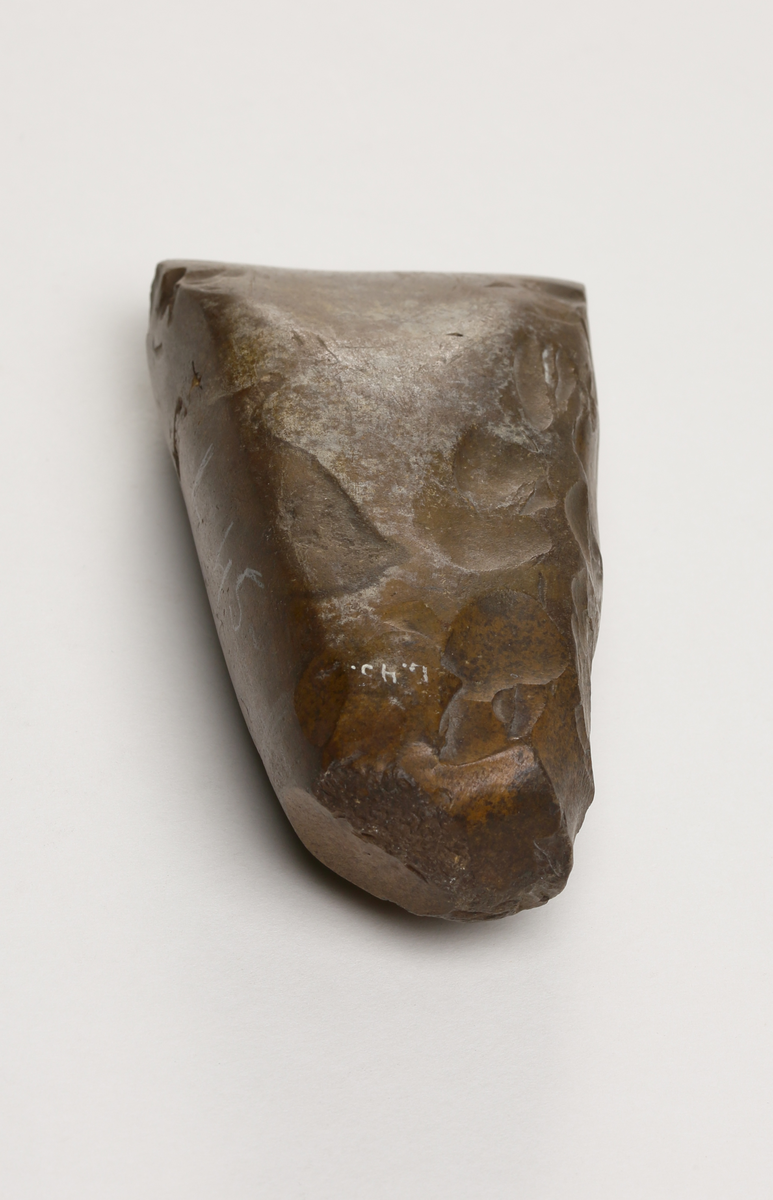 Flintyxa av brun flinta, tjocknackig, slipad och svallad, svagt håleggad. Kvadratisk genomskärning.