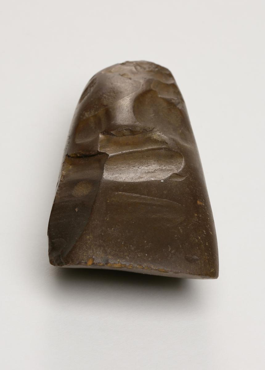 Flintyxa av brun flinta, tjocknackig, slipad och svallad, svagt håleggad. Kvadratisk genomskärning.