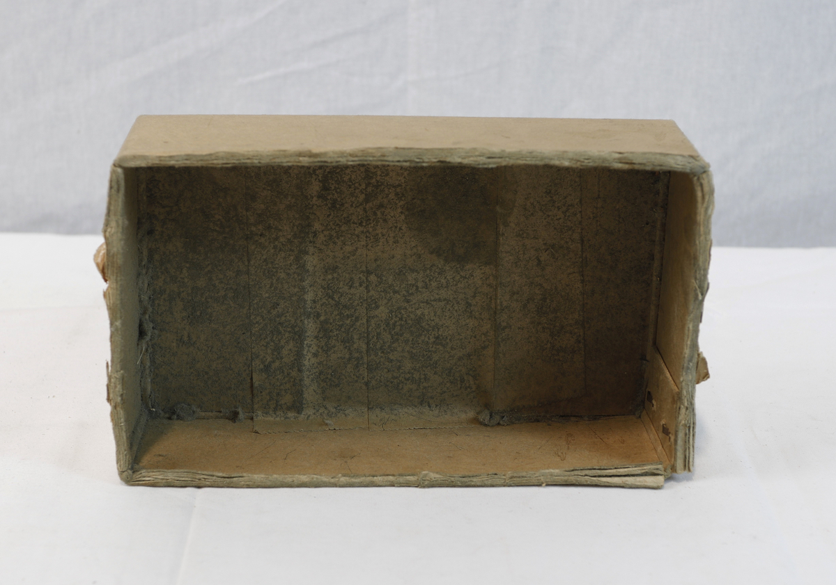 Del av pappeske. Esken har brun papirtape med logo. Brukt til enten oppbevaring eller innpakning av gullsmedgjenstander.