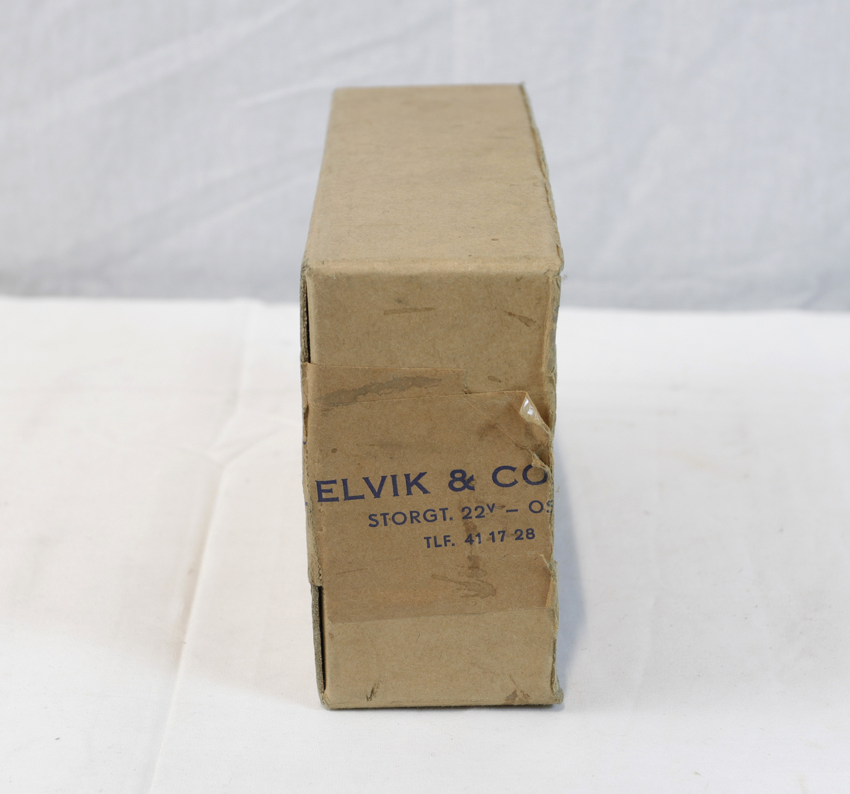 Del av pappeske. Esken har brun papirtape med logo. Brukt til enten oppbevaring eller innpakning av gullsmedgjenstander.