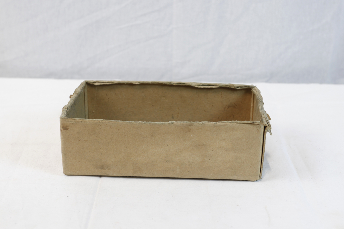 Del av pappeske. Esken har brun papirtape med logo. Brukt til enten oppbevaring eller innpakning av gullsmedgjenstander.