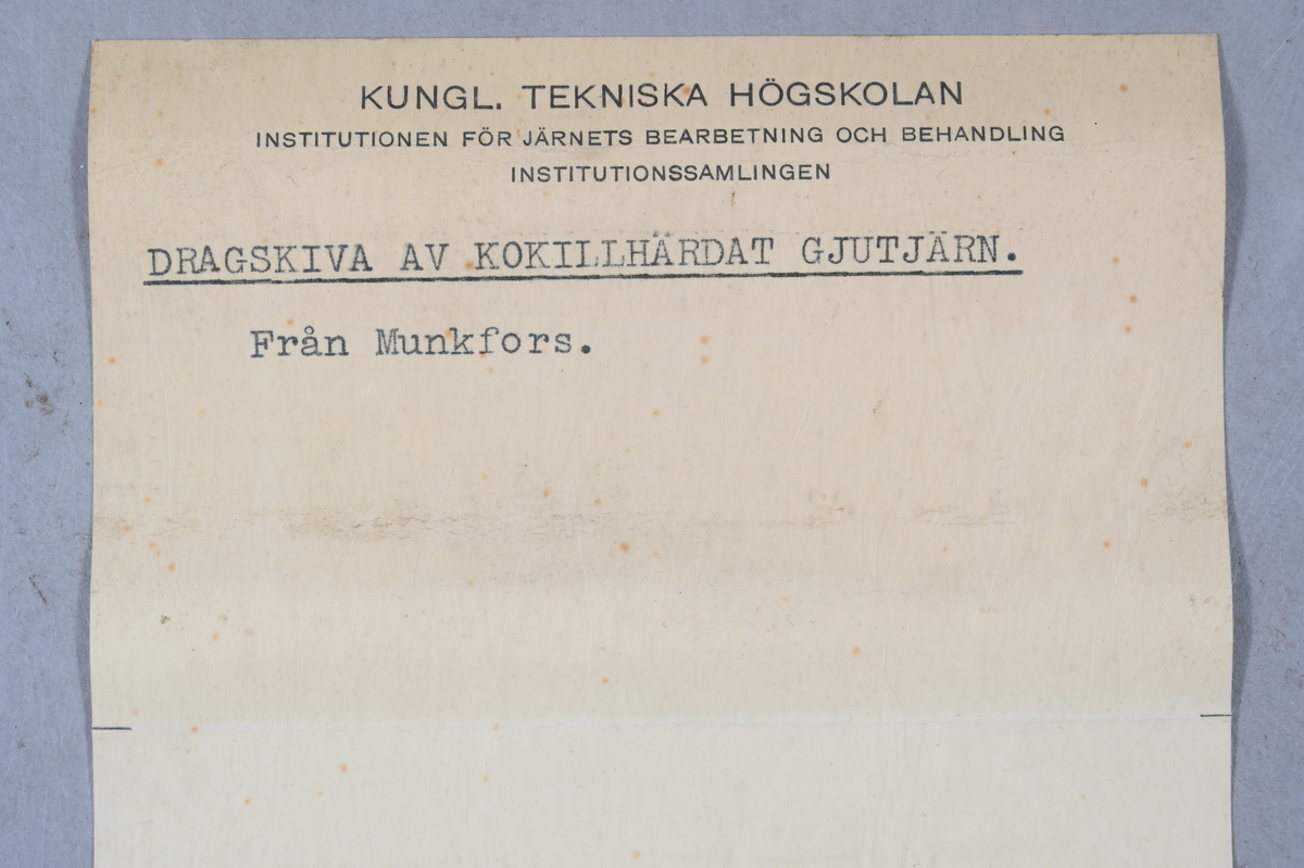 Prov på dragskiva av kokillhärdat gjutjärn. Provet kommer från Munkfors. Tillhörande lapp med samma notering.
