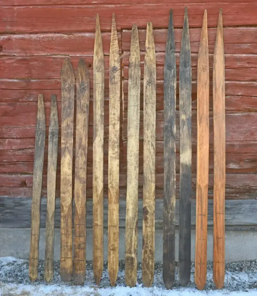 Handgjorda träskidor står lutade mot en faluröd timmervägg.