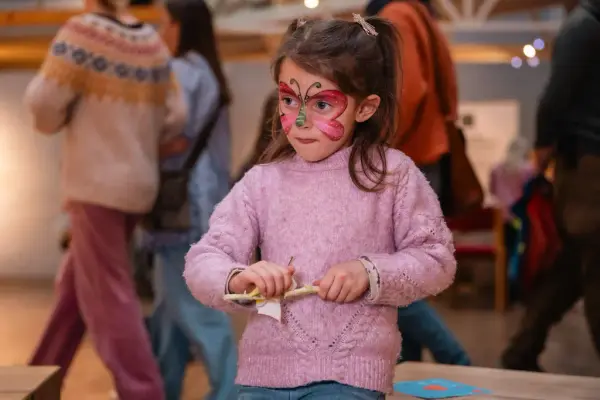 Jente med malt sommerfugl i ansiktet pusser med sandpapir på en pinne