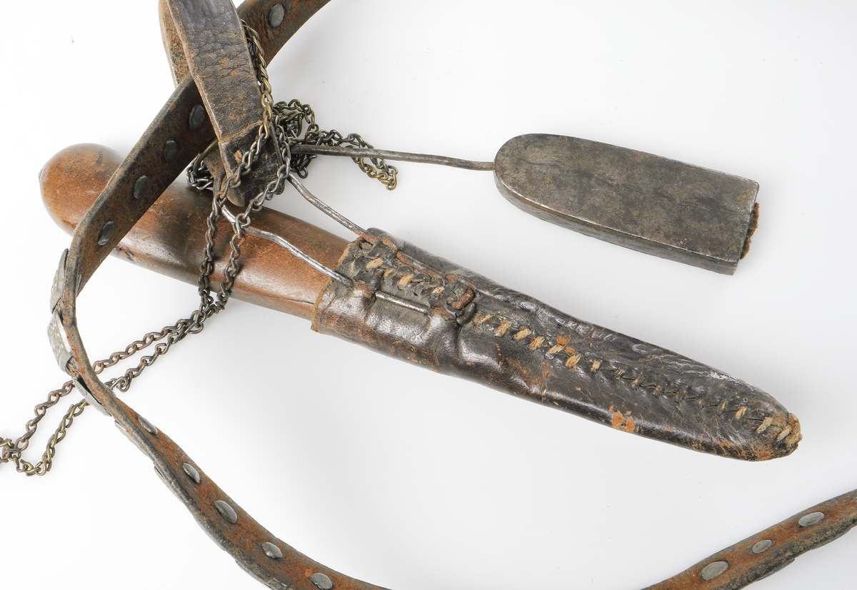 Så kallat kvinnobälte med kniv och nålhus från Dalarna. Bältet är gjort av läder och är prytt med små gjutna tennplattor. Nålhus och kniv är av järn, knivskaftet tillverkat av päronträ med mässingsdetalj ned mot knivbladet.