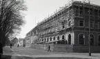 Sparbanksfastigheten på Kungsgatan, kv. Sunaman, under uppförande, med en vy utmed Kungsgatan med järnvägsstationen i fonden, bakom vilken läroverket tornar upp sig.