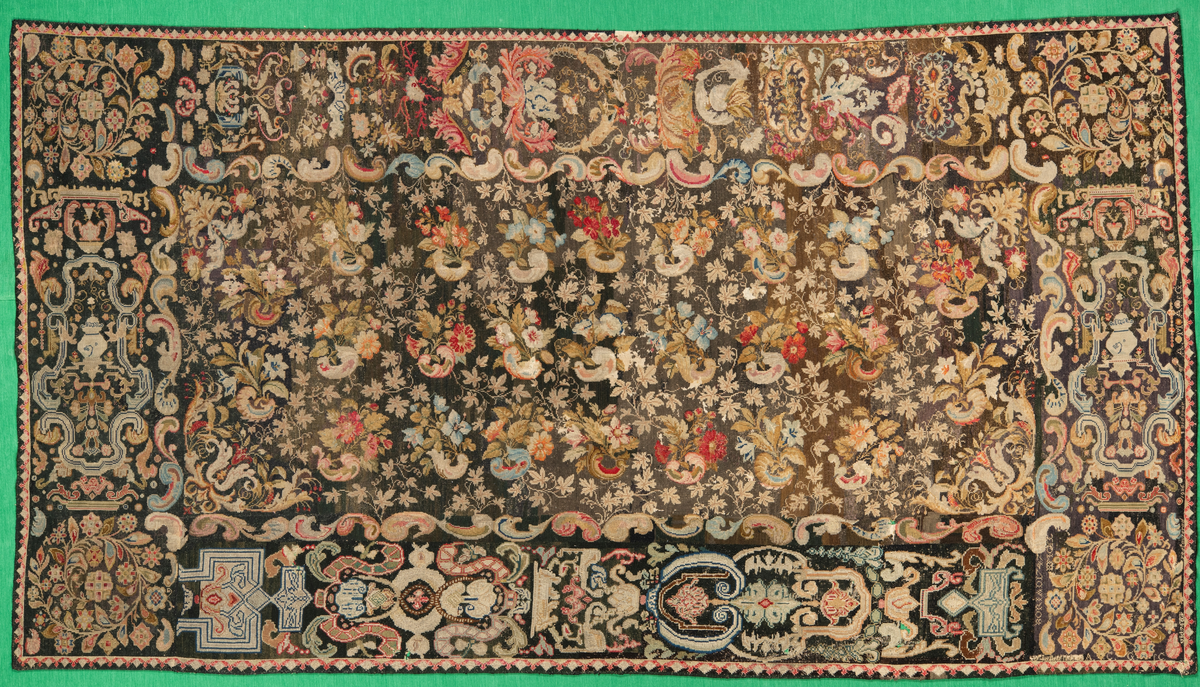 Linbotten med broderier i framför allt ull. Vissa detaljer troligen gjorda i silke. Lagningarna utförda i ull och bomull. Broderiet gjort i korsstygn. De äldsta delarna (bården) är gjorda i olika stora stygn varför ytans karaktär varierar. Mönster som påminner om pompeijansk stil med bland annat kartusher, urnor och växtornament. Mittpartiet inramat med roccaier eller akantusblad, blombotten med liljor och rosor samt vinrankor. Längst ena långsidan även inslag av korall. Hörn med spiralformade blomstergirlanger, dessa med drag av folkligt broderi.
Brunsvart botten, ojämt blekt. Merparten beigegröna nyanser på växtornamenten. Blåa och röda inslag där vissa röda delar skulle kunna vara anilinfärg, troligen i övrigt växtfärg.