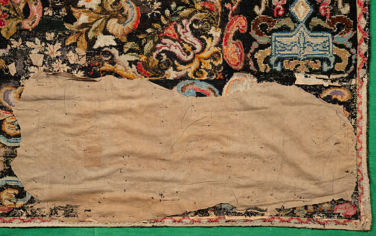 Linbotten med broderier i framför allt ull. Vissa detaljer troligen gjorda i silke. Lagningarna utförda i ull och bomull. Broderiet gjort i korsstygn. De äldsta delarna (bården) är gjorda i olika stora stygn varför ytans karaktär varierar. Mönster som påminner om pompeijansk stil med bland annat kartusher, urnor och växtornament. Mittpartiet inramat med roccaier eller akantusblad, blombotten med liljor och rosor samt vinrankor. Längst ena långsidan även inslag av korall. Hörn med spiralformade blomstergirlanger, dessa med drag av folkligt broderi.
Brunsvart botten, ojämt blekt. Merparten beigegröna nyanser på växtornamenten. Blåa och röda inslag där vissa röda delar skulle kunna vara anilinfärg, troligen i övrigt växtfärg.