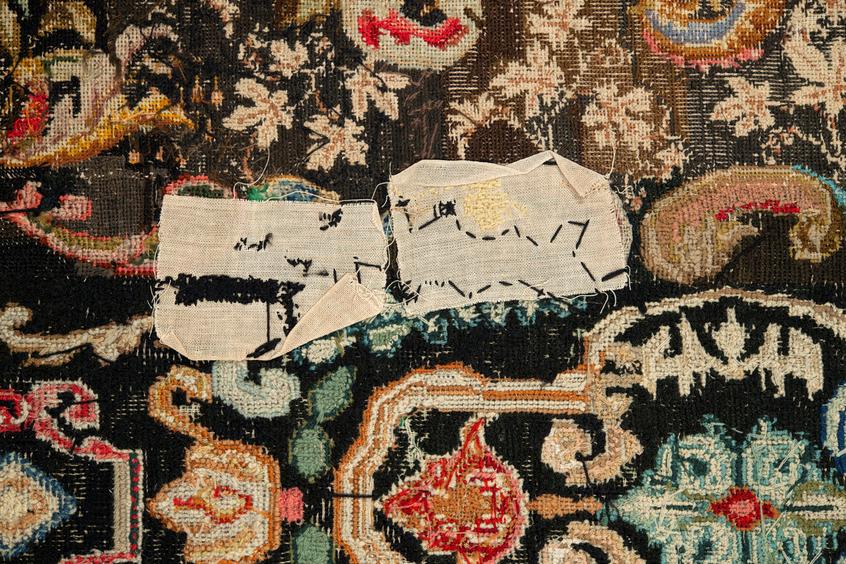 Linbotten med broderier i framför allt ull. Vissa detaljer troligen gjorda i silke. Lagningarna utförda i ull och bomull. Broderiet gjort i korsstygn. De äldsta delarna (bården) är gjorda i olika stora stygn varför ytans karaktär varierar. Mönster som påminner om pompeijansk stil med bland annat kartusher, urnor och växtornament. Mittpartiet inramat med roccaier eller akantusblad, blombotten med liljor och rosor samt vinrankor. Längst ena långsidan även inslag av korall. Hörn med spiralformade blomstergirlanger, dessa med drag av folkligt broderi.
Brunsvart botten, ojämt blekt. Merparten beigegröna nyanser på växtornamenten. Blåa och röda inslag där vissa röda delar skulle kunna vara anilinfärg, troligen i övrigt växtfärg.