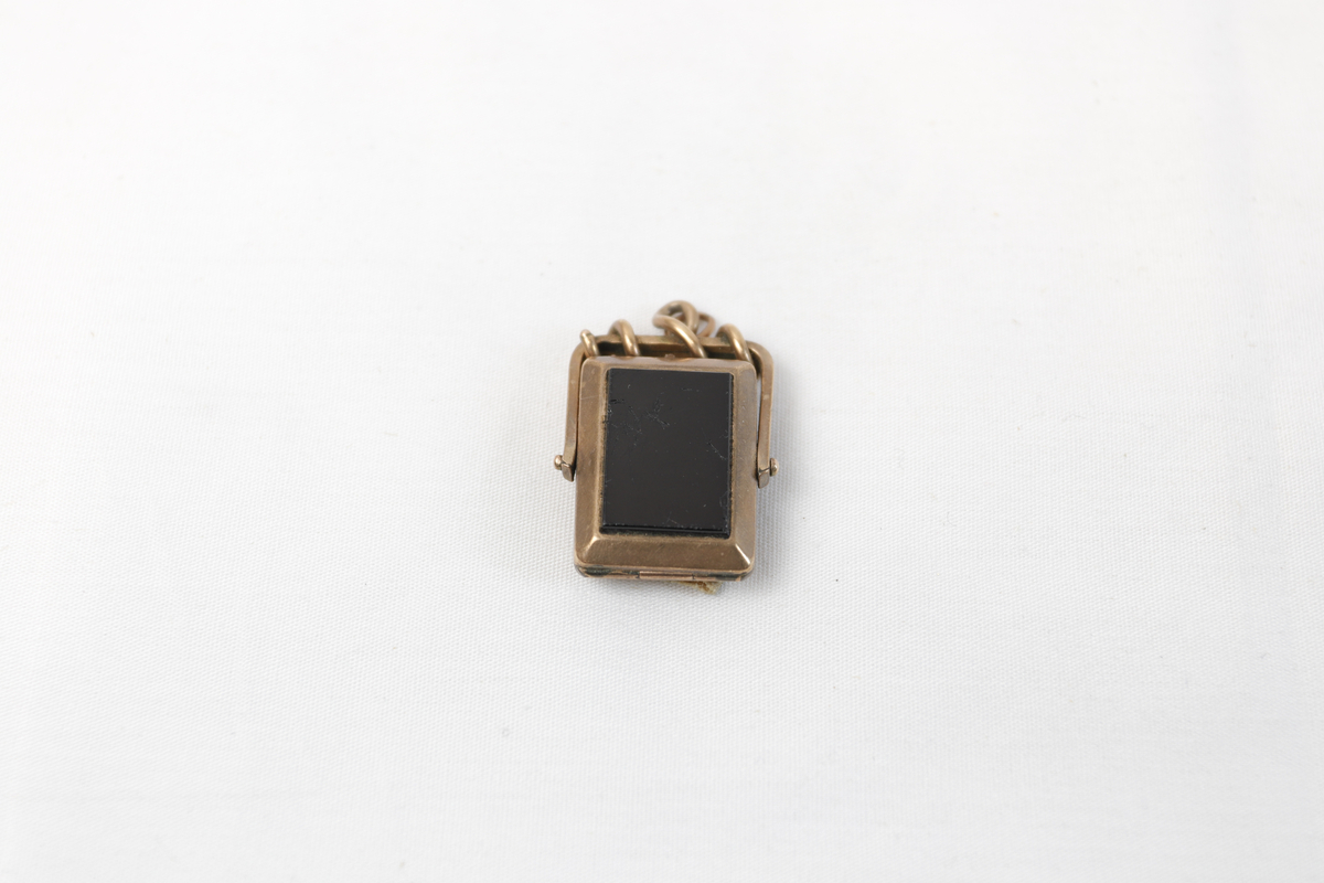 Smykkeanheng med innrissede bokstaver og tall langs sidene.