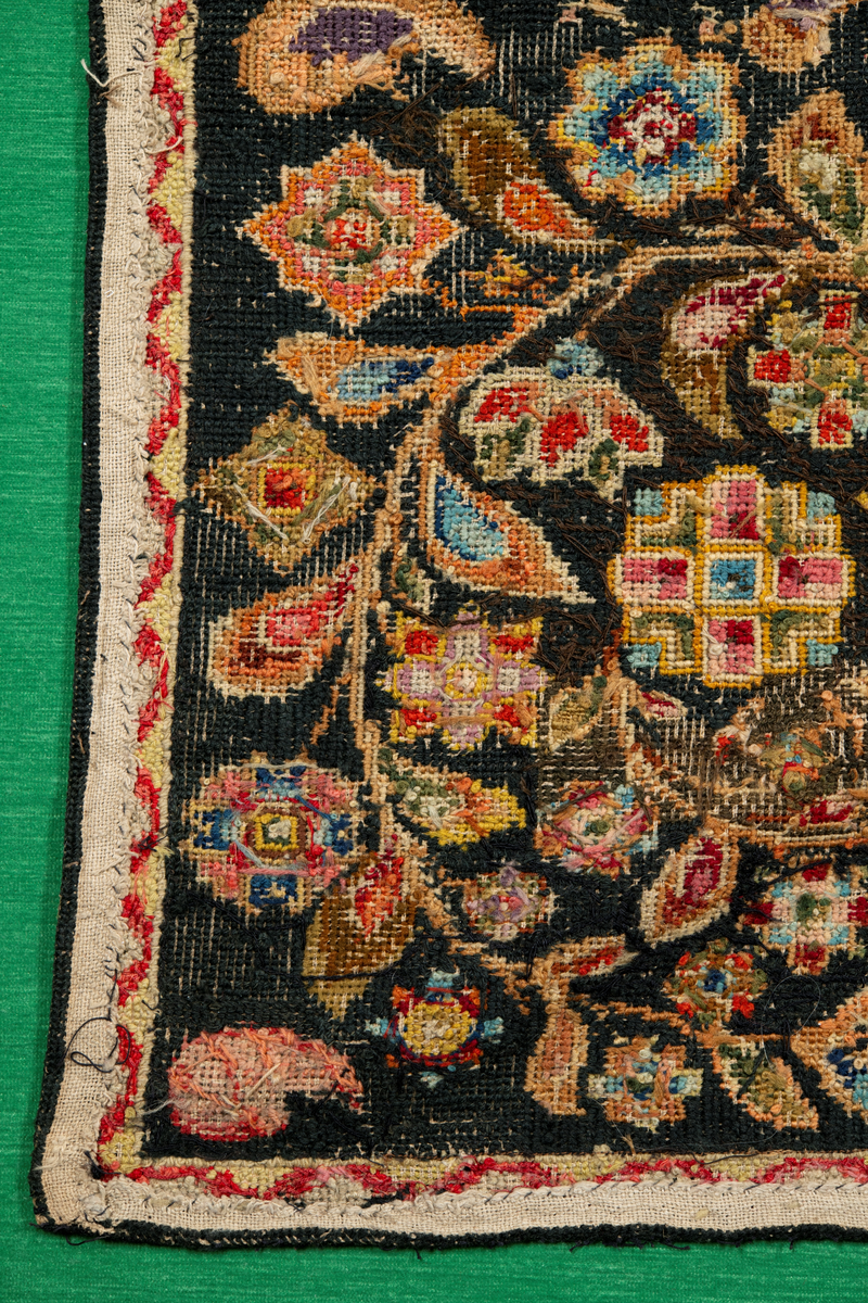 Linbotten med broderier i framför allt ull. Vissa detaljer troligen gjorda i silke. Lagningarna utförda i ull och bomull. Broderiet gjort i korsstygn. De äldsta delarna (bården) är gjorda i olika stora stygn varför ytans karaktär varierar. Mönster som påminner om pompeijansk stil med bland annat kartusher, urnor och växtornament. Mittpartiet inramat med roccaier eller akantusblad, blombotten med liljor och rosor samt vinrankor. Längst ena långsidan även inslag av korall. Hörn med spiralformade blomstergirlanger, dessa med drag av folkligt broderi.
Brunsvart botten, ojämt blekt. Merparten beigegröna nyanser på växtornamenten. Blåa och röda inslag där vissa röda delar skulle kunna vara anilinfärg, troligen i övrigt växtfärg.