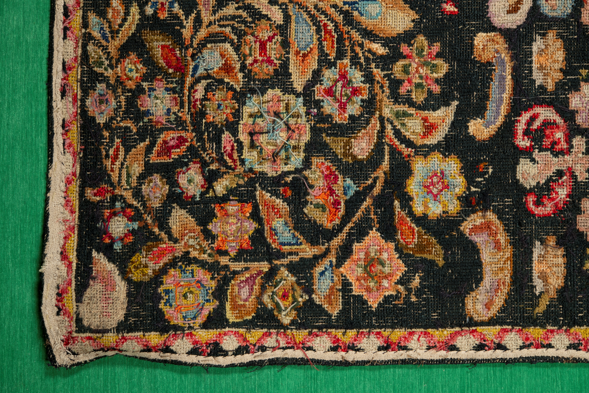 Linbotten med broderier i framför allt ull. Vissa detaljer troligen gjorda i silke. Lagningarna utförda i ull och bomull. Broderiet gjort i korsstygn. De äldsta delarna (bården) är gjorda i olika stora stygn varför ytans karaktär varierar. Mönster som påminner om pompeijansk stil med bland annat kartusher, urnor och växtornament. Mittpartiet inramat med roccaier eller akantusblad, blombotten med liljor och rosor samt vinrankor. Längst ena långsidan även inslag av korall. Hörn med spiralformade blomstergirlanger, dessa med drag av folkligt broderi.
Brunsvart botten, ojämt blekt. Merparten beigegröna nyanser på växtornamenten. Blåa och röda inslag där vissa röda delar skulle kunna vara anilinfärg, troligen i övrigt växtfärg.