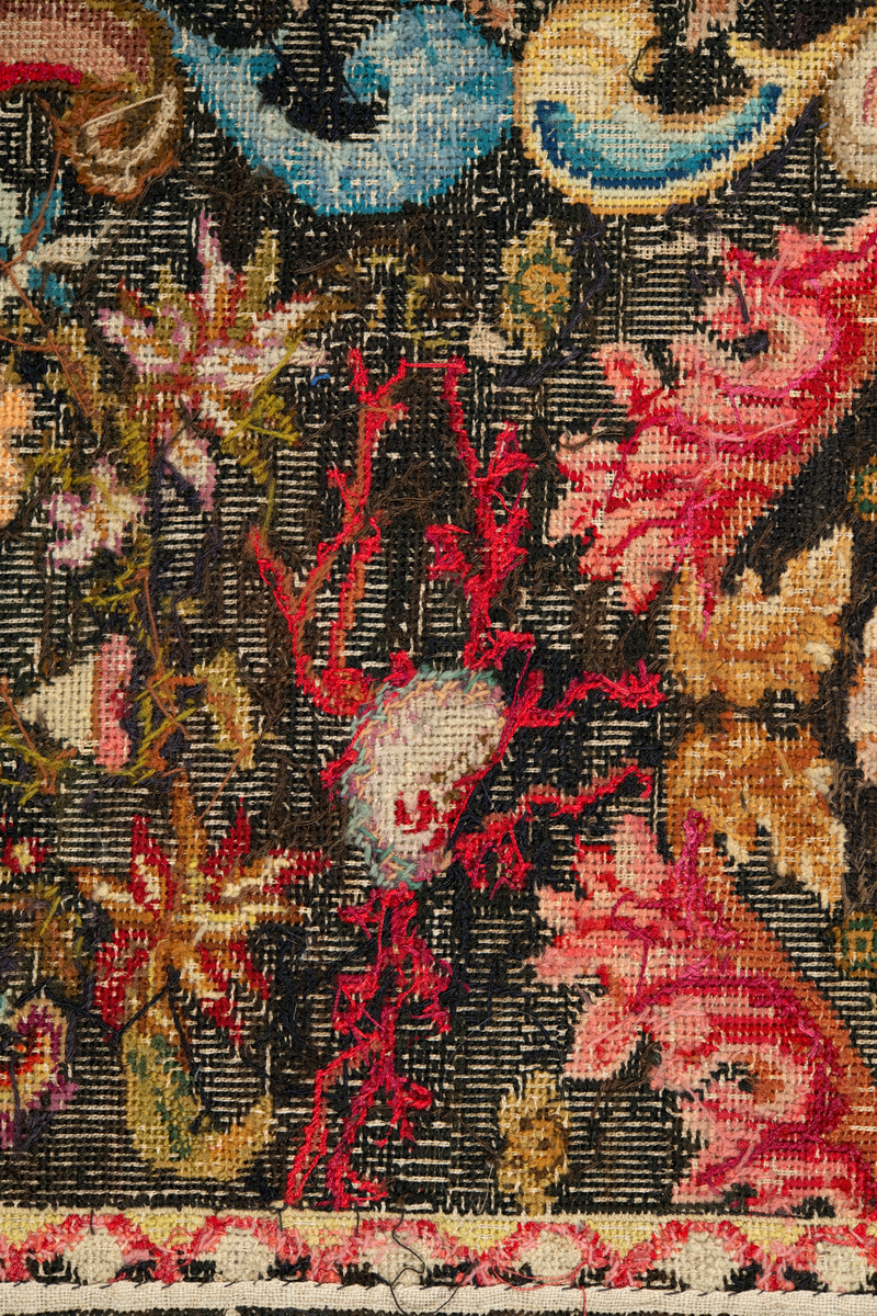 Linbotten med broderier i framför allt ull. Vissa detaljer troligen gjorda i silke. Lagningarna utförda i ull och bomull. Broderiet gjort i korsstygn. De äldsta delarna (bården) är gjorda i olika stora stygn varför ytans karaktär varierar. Mönster som påminner om pompeijansk stil med bland annat kartusher, urnor och växtornament. Mittpartiet inramat med roccaier eller akantusblad, blombotten med liljor och rosor samt vinrankor. Längst ena långsidan även inslag av korall. Hörn med spiralformade blomstergirlanger, dessa med drag av folkligt broderi.
Brunsvart botten, ojämt blekt. Merparten beigegröna nyanser på växtornamenten. Blåa och röda inslag där vissa röda delar skulle kunna vara anilinfärg, troligen i övrigt växtfärg.