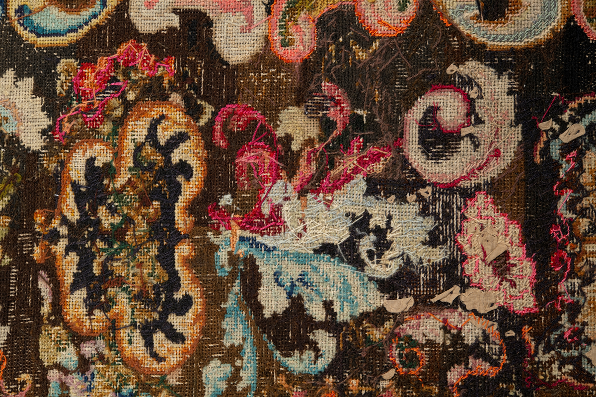 Linbotten med broderier i framför allt ull. Vissa detaljer troligen gjorda i silke. Lagningarna utförda i ull och bomull. Broderiet gjort i korsstygn. De äldsta delarna (bården) är gjorda i olika stora stygn varför ytans karaktär varierar. Mönster som påminner om pompeijansk stil med bland annat kartusher, urnor och växtornament. Mittpartiet inramat med roccaier eller akantusblad, blombotten med liljor och rosor samt vinrankor. Längst ena långsidan även inslag av korall. Hörn med spiralformade blomstergirlanger, dessa med drag av folkligt broderi.
Brunsvart botten, ojämt blekt. Merparten beigegröna nyanser på växtornamenten. Blåa och röda inslag där vissa röda delar skulle kunna vara anilinfärg, troligen i övrigt växtfärg.