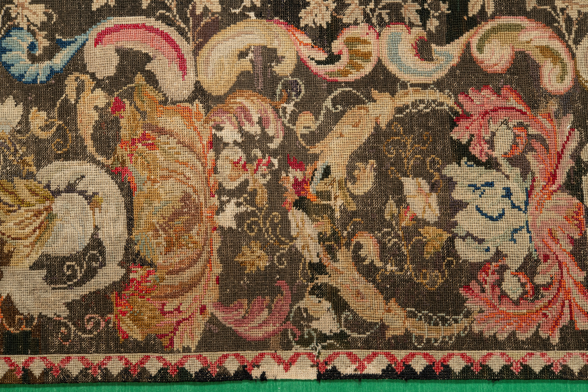 Linbotten med broderier i framför allt ull. Vissa detaljer troligen gjorda i silke. Lagningarna utförda i ull och bomull. Broderiet gjort i korsstygn. De äldsta delarna (bården) är gjorda i olika stora stygn varför ytans karaktär varierar. Mönster som påminner om pompeijansk stil med bland annat kartusher, urnor och växtornament. Mittpartiet inramat med roccaier eller akantusblad, blombotten med liljor och rosor samt vinrankor. Längst ena långsidan även inslag av korall. Hörn med spiralformade blomstergirlanger, dessa med drag av folkligt broderi.
Brunsvart botten, ojämt blekt. Merparten beigegröna nyanser på växtornamenten. Blåa och röda inslag där vissa röda delar skulle kunna vara anilinfärg, troligen i övrigt växtfärg.