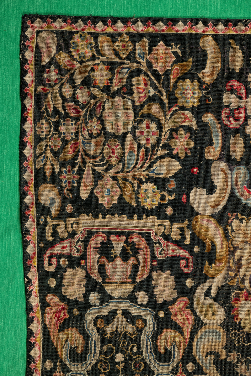 Linbotten med broderier i framför allt ull. Vissa detaljer troligen gjorda i silke. Lagningarna utförda i ull och bomull. Broderiet gjort i korsstygn. De äldsta delarna (bården) är gjorda i olika stora stygn varför ytans karaktär varierar. Mönster som påminner om pompeijansk stil med bland annat kartusher, urnor och växtornament. Mittpartiet inramat med roccaier eller akantusblad, blombotten med liljor och rosor samt vinrankor. Längst ena långsidan även inslag av korall. Hörn med spiralformade blomstergirlanger, dessa med drag av folkligt broderi.
Brunsvart botten, ojämt blekt. Merparten beigegröna nyanser på växtornamenten. Blåa och röda inslag där vissa röda delar skulle kunna vara anilinfärg, troligen i övrigt växtfärg.