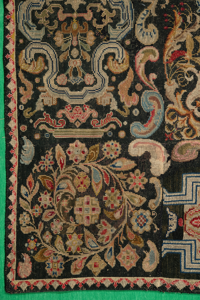 Linbotten med broderier i framför allt ull. Vissa detaljer troligen gjorda i silke. Lagningarna utförda i ull och bomull. Broderiet gjort i korsstygn. De äldsta delarna (bården) är gjorda i olika stora stygn varför ytans karaktär varierar. Mönster som påminner om pompeijansk stil med bland annat kartusher, urnor och växtornament. Mittpartiet inramat med roccaier eller akantusblad, blombotten med liljor och rosor samt vinrankor. Längst ena långsidan även inslag av korall. Hörn med spiralformade blomstergirlanger, dessa med drag av folkligt broderi.
Brunsvart botten, ojämt blekt. Merparten beigegröna nyanser på växtornamenten. Blåa och röda inslag där vissa röda delar skulle kunna vara anilinfärg, troligen i övrigt växtfärg.