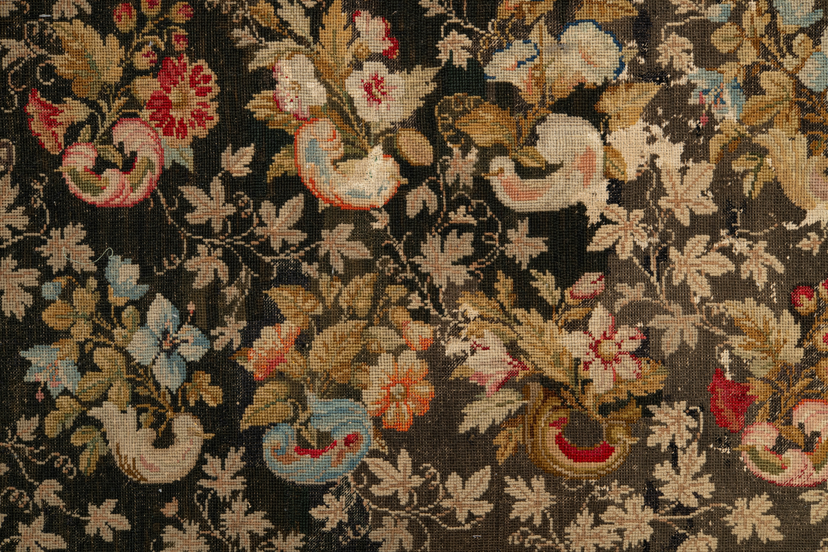 Linbotten med broderier i framför allt ull. Vissa detaljer troligen gjorda i silke. Lagningarna utförda i ull och bomull. Broderiet gjort i korsstygn. De äldsta delarna (bården) är gjorda i olika stora stygn varför ytans karaktär varierar. Mönster som påminner om pompeijansk stil med bland annat kartusher, urnor och växtornament. Mittpartiet inramat med roccaier eller akantusblad, blombotten med liljor och rosor samt vinrankor. Längst ena långsidan även inslag av korall. Hörn med spiralformade blomstergirlanger, dessa med drag av folkligt broderi.
Brunsvart botten, ojämt blekt. Merparten beigegröna nyanser på växtornamenten. Blåa och röda inslag där vissa röda delar skulle kunna vara anilinfärg, troligen i övrigt växtfärg.