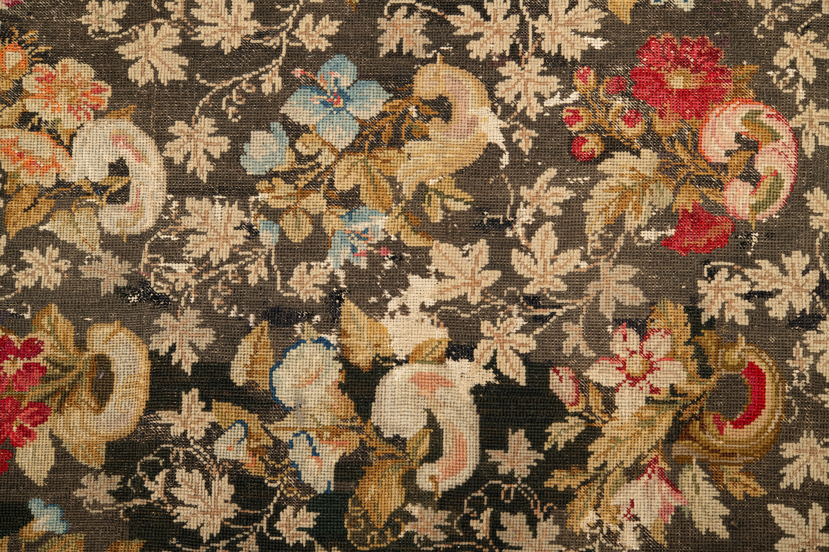 Linbotten med broderier i framför allt ull. Vissa detaljer troligen gjorda i silke. Lagningarna utförda i ull och bomull. Broderiet gjort i korsstygn. De äldsta delarna (bården) är gjorda i olika stora stygn varför ytans karaktär varierar. Mönster som påminner om pompeijansk stil med bland annat kartusher, urnor och växtornament. Mittpartiet inramat med roccaier eller akantusblad, blombotten med liljor och rosor samt vinrankor. Längst ena långsidan även inslag av korall. Hörn med spiralformade blomstergirlanger, dessa med drag av folkligt broderi.
Brunsvart botten, ojämt blekt. Merparten beigegröna nyanser på växtornamenten. Blåa och röda inslag där vissa röda delar skulle kunna vara anilinfärg, troligen i övrigt växtfärg.