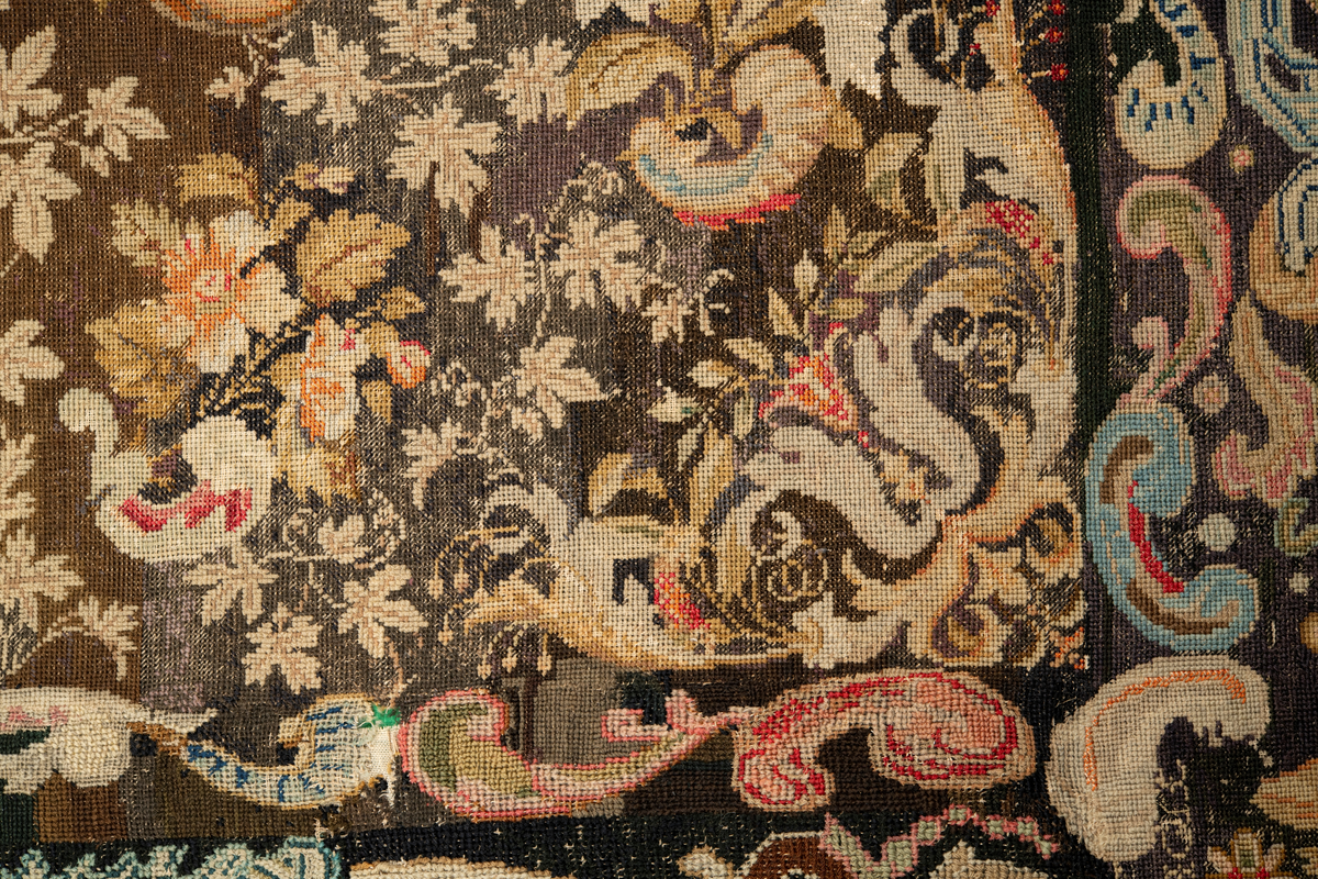 Linbotten med broderier i framför allt ull. Vissa detaljer troligen gjorda i silke. Lagningarna utförda i ull och bomull. Broderiet gjort i korsstygn. De äldsta delarna (bården) är gjorda i olika stora stygn varför ytans karaktär varierar. Mönster som påminner om pompeijansk stil med bland annat kartusher, urnor och växtornament. Mittpartiet inramat med roccaier eller akantusblad, blombotten med liljor och rosor samt vinrankor. Längst ena långsidan även inslag av korall. Hörn med spiralformade blomstergirlanger, dessa med drag av folkligt broderi.
Brunsvart botten, ojämt blekt. Merparten beigegröna nyanser på växtornamenten. Blåa och röda inslag där vissa röda delar skulle kunna vara anilinfärg, troligen i övrigt växtfärg.