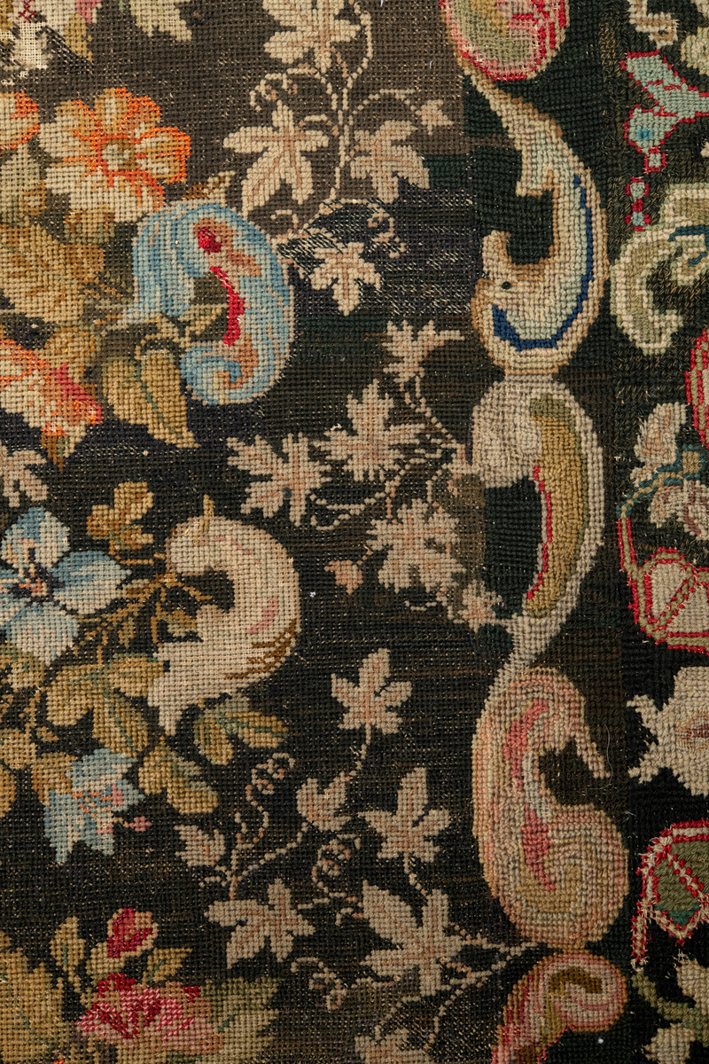 Linbotten med broderier i framför allt ull. Vissa detaljer troligen gjorda i silke. Lagningarna utförda i ull och bomull. Broderiet gjort i korsstygn. De äldsta delarna (bården) är gjorda i olika stora stygn varför ytans karaktär varierar. Mönster som påminner om pompeijansk stil med bland annat kartusher, urnor och växtornament. Mittpartiet inramat med roccaier eller akantusblad, blombotten med liljor och rosor samt vinrankor. Längst ena långsidan även inslag av korall. Hörn med spiralformade blomstergirlanger, dessa med drag av folkligt broderi.
Brunsvart botten, ojämt blekt. Merparten beigegröna nyanser på växtornamenten. Blåa och röda inslag där vissa röda delar skulle kunna vara anilinfärg, troligen i övrigt växtfärg.