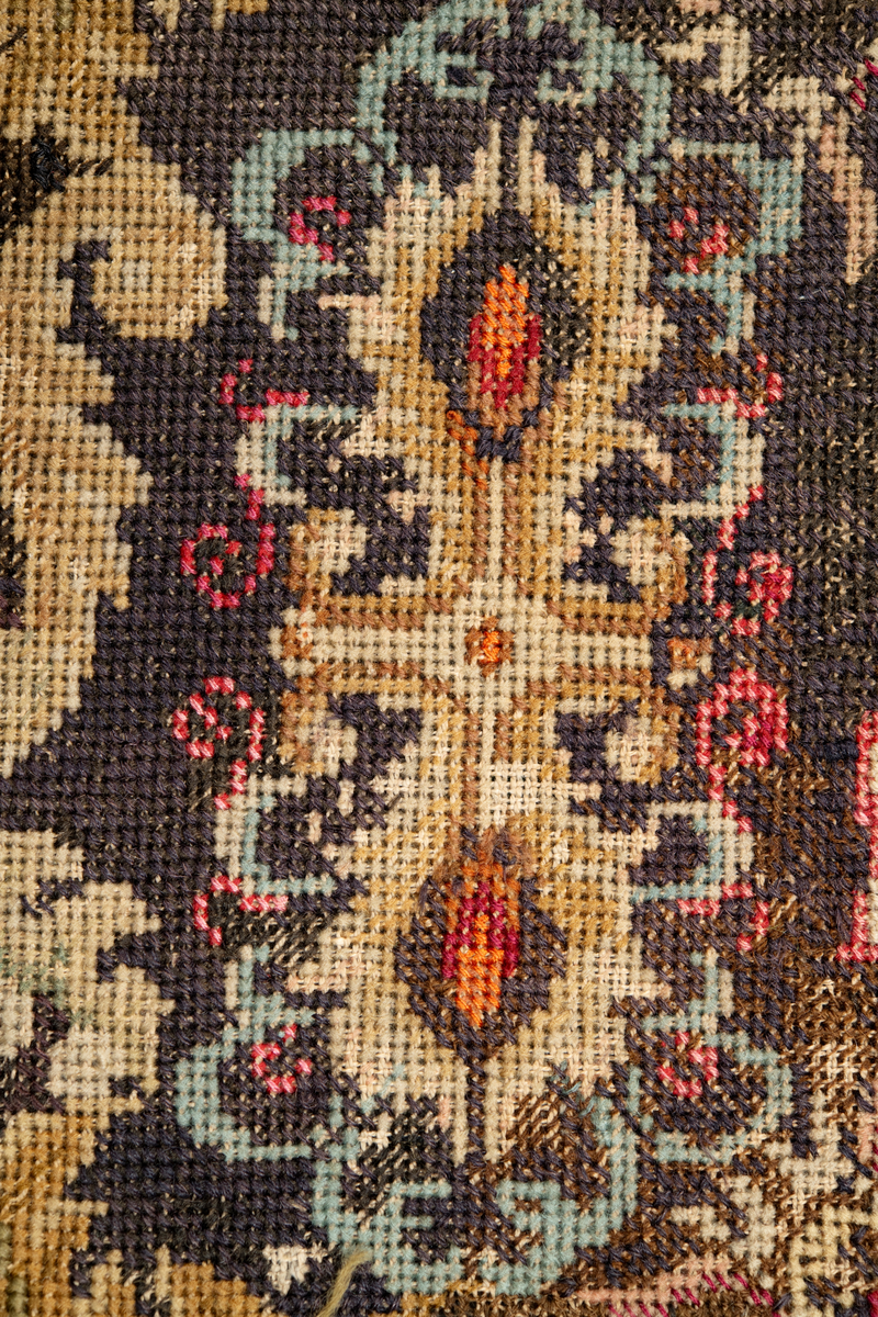 Linbotten med broderier i framför allt ull. Vissa detaljer troligen gjorda i silke. Lagningarna utförda i ull och bomull. Broderiet gjort i korsstygn. De äldsta delarna (bården) är gjorda i olika stora stygn varför ytans karaktär varierar. Mönster som påminner om pompeijansk stil med bland annat kartusher, urnor och växtornament. Mittpartiet inramat med roccaier eller akantusblad, blombotten med liljor och rosor samt vinrankor. Längst ena långsidan även inslag av korall. Hörn med spiralformade blomstergirlanger, dessa med drag av folkligt broderi.
Brunsvart botten, ojämt blekt. Merparten beigegröna nyanser på växtornamenten. Blåa och röda inslag där vissa röda delar skulle kunna vara anilinfärg, troligen i övrigt växtfärg.