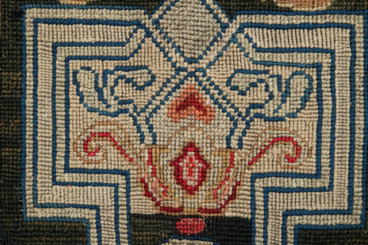 Linbotten med broderier i framför allt ull. Vissa detaljer troligen gjorda i silke. Lagningarna utförda i ull och bomull. Broderiet gjort i korsstygn. De äldsta delarna (bården) är gjorda i olika stora stygn varför ytans karaktär varierar. Mönster som påminner om pompeijansk stil med bland annat kartusher, urnor och växtornament. Mittpartiet inramat med roccaier eller akantusblad, blombotten med liljor och rosor samt vinrankor. Längst ena långsidan även inslag av korall. Hörn med spiralformade blomstergirlanger, dessa med drag av folkligt broderi.
Brunsvart botten, ojämt blekt. Merparten beigegröna nyanser på växtornamenten. Blåa och röda inslag där vissa röda delar skulle kunna vara anilinfärg, troligen i övrigt växtfärg.