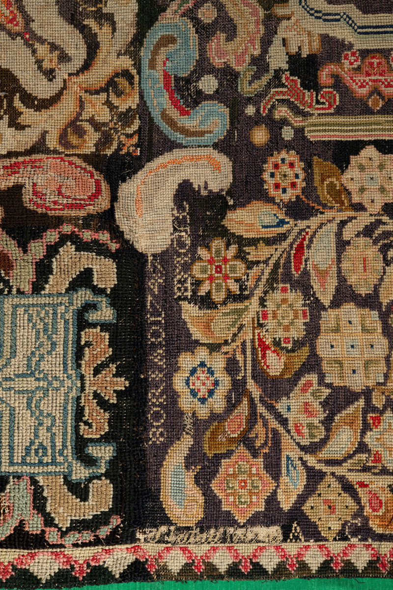 Linbotten med broderier i framför allt ull. Vissa detaljer troligen gjorda i silke. Lagningarna utförda i ull och bomull. Broderiet gjort i korsstygn. De äldsta delarna (bården) är gjorda i olika stora stygn varför ytans karaktär varierar. Mönster som påminner om pompeijansk stil med bland annat kartusher, urnor och växtornament. Mittpartiet inramat med roccaier eller akantusblad, blombotten med liljor och rosor samt vinrankor. Längst ena långsidan även inslag av korall. Hörn med spiralformade blomstergirlanger, dessa med drag av folkligt broderi.
Brunsvart botten, ojämt blekt. Merparten beigegröna nyanser på växtornamenten. Blåa och röda inslag där vissa röda delar skulle kunna vara anilinfärg, troligen i övrigt växtfärg.