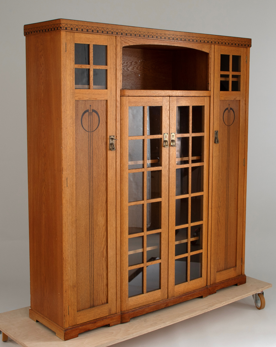 Buffet i bonet eik, dekorert med intarsia av ibenholt (?) og messingbeslag. Møblementet har en streng arkitektonisk oppbyggning, og preges av et spill mellom vertikale og horisontale volumer. Midtpartiet består av et vitrineskap med dobbeltdører, dekorert med felt av krysspostvinduer. Det rektangulære overskapet har svakt buet innramming. På hver side av midtpartiet to smale vertikale skap, hvis dører er dekorert med intarsia i form av geometriske jugendornamenter. Buffeten avsluttes med et profilert toppstykke.