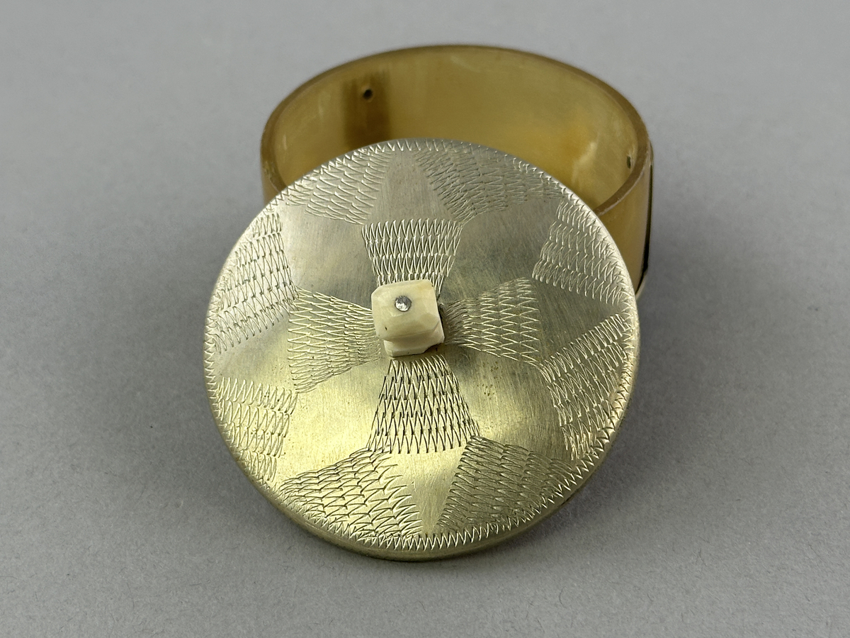 Saltkar, i form av rund burk med lock, i silversmide utfört av resandefolk. Metall i botten och lock med graverat mönster. Kohorn mellan botten och lock, ben i fötter och knopp. Till saltkaret hör en sked, se inv.nr 0875.