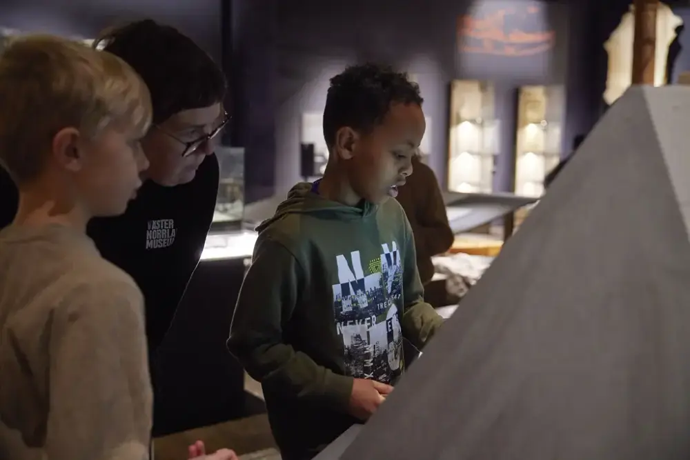 En grupp barn och en pedagog spelar Crafthunter i utställningen Forntidsresan.