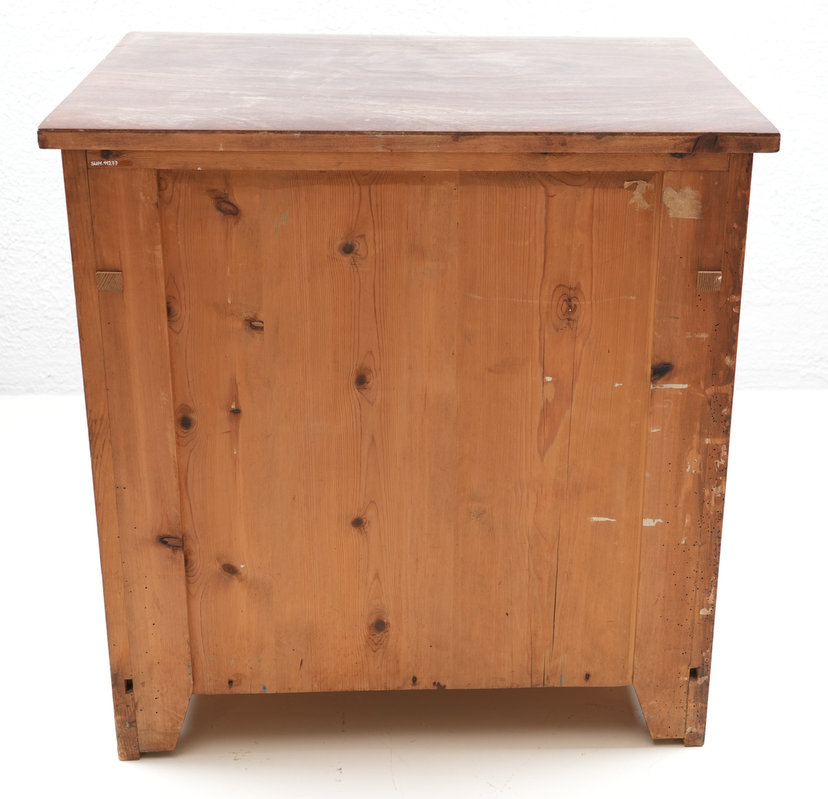 Brunbeisa kommode i heiltre. Ei skuffe øverst med messinghandtak. Under skuffa er det eit skap med doble skapdører og messinghandtak. Enkel profil på skapdørene. Ei hylleplate inni av heiltre. Kommoden står på fire bein. 