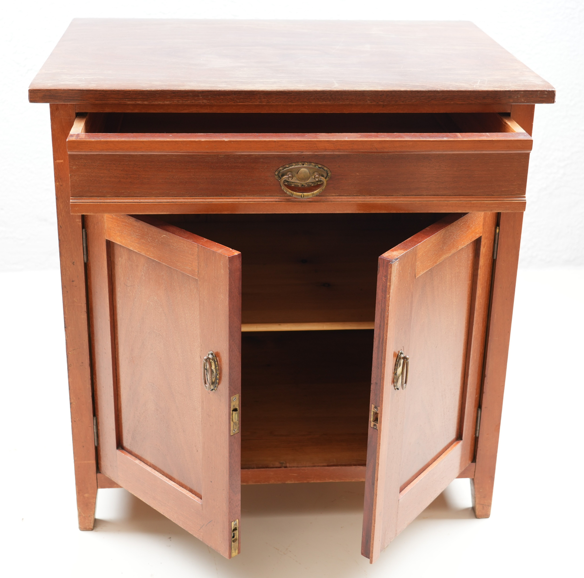 Brunbeisa kommode i heiltre. Ei skuffe øverst med messinghandtak. Under skuffa er det eit skap med doble skapdører og messinghandtak. Enkel profil på skapdørene. Ei hylleplate inni av heiltre. Kommoden står på fire bein. 