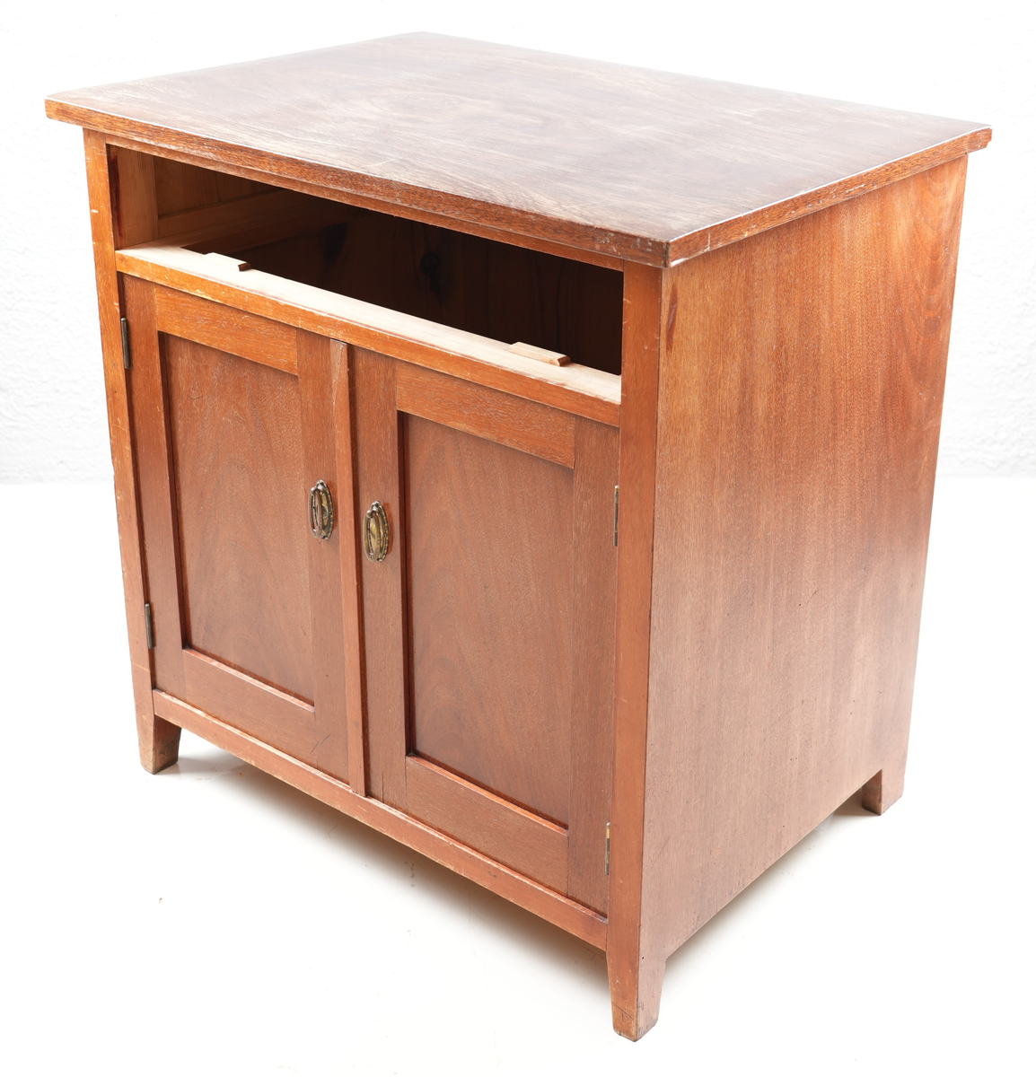 Brunbeisa kommode i heiltre. Ei skuffe øverst med messinghandtak. Under skuffa er det eit skap med doble skapdører og messinghandtak. Enkel profil på skapdørene. Ei hylleplate inni av heiltre. Kommoden står på fire bein. 