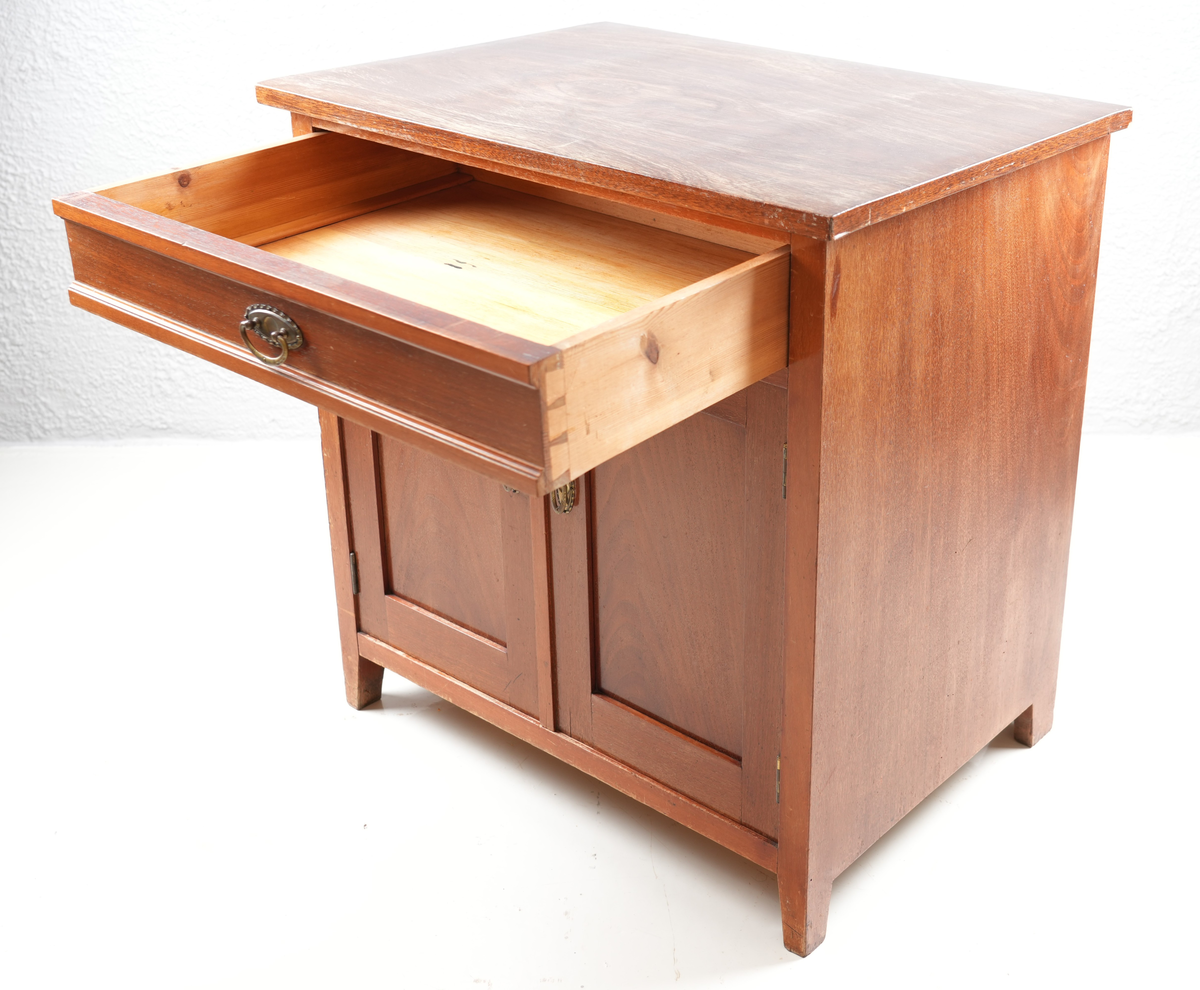 Brunbeisa kommode i heiltre. Ei skuffe øverst med messinghandtak. Under skuffa er det eit skap med doble skapdører og messinghandtak. Enkel profil på skapdørene. Ei hylleplate inni av heiltre. Kommoden står på fire bein. 