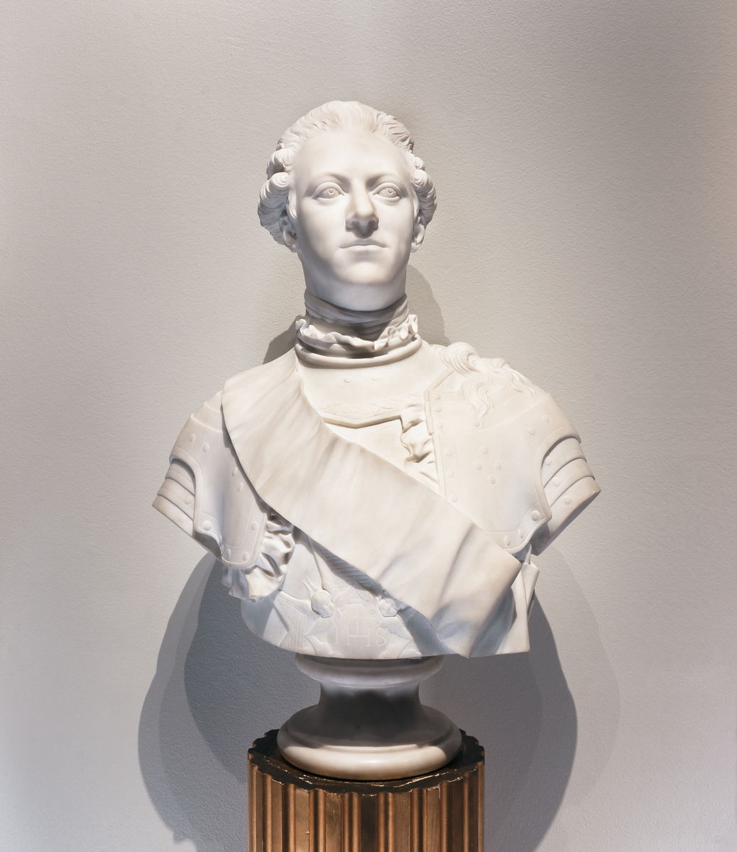 Marmorbyst föreställande Kung Gustav III, "Copia fatta da M. Bacci. Florens", dvs marmorkopia efter gipsoriginal av J T Sergel från 1779. Står på hög gustaviansk piedestal, med vertikala hålkäler och lagerkrans nertill kring foten. Piedestalen står på lågt fyrkantigt podium.
Kopia utförd av M. Bacci Florens. Montering/Ram: Originalpiedestal från ca 1800