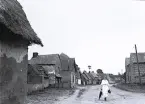 Foto av en byväg kantad med små hus, vissa med halmtak i Normandie, 1921.
