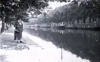 Foto av en kvinna som står vid en kajkant med kanalbåtar i bakgrunden, troligen i Amsterdam, 1924-25.