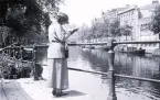 Foto av en kvinna som står och läser en bok vid en kajkant, troligen i Amsterdam, 1924-25.