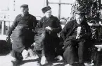 Foto av tre äldre män som sitter ner och är klädda i rockar och de traditionella träskor som var vanliga i nederländerna, 1924-25.
